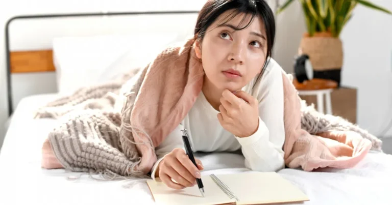 ベッドで考え事をしながら書き物をする女性